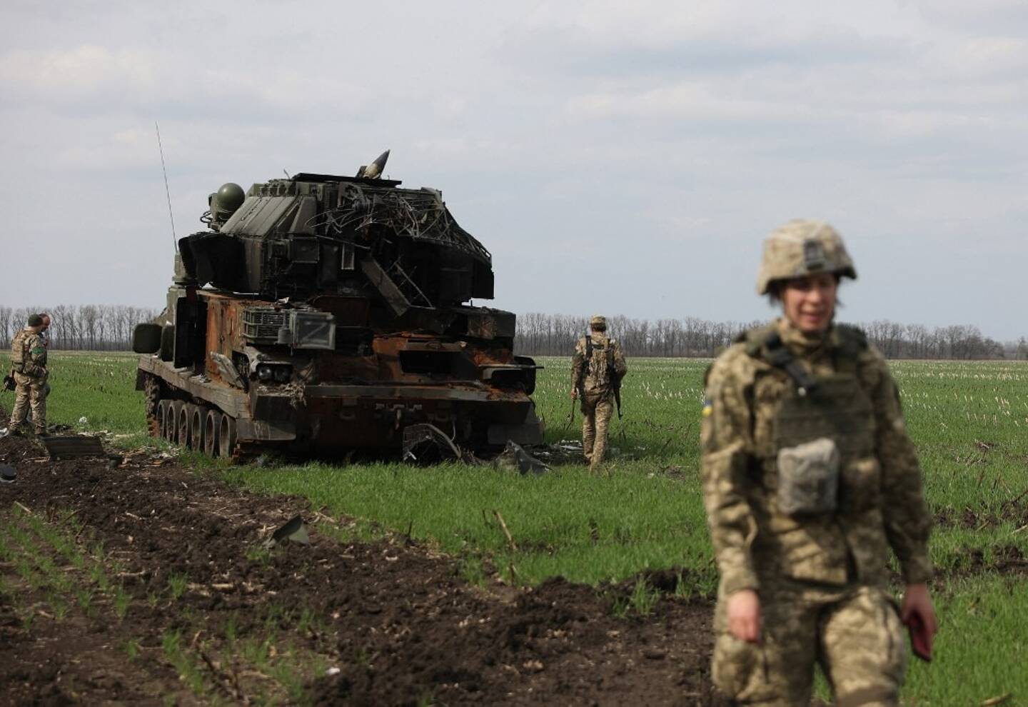 Des soldats ukrainiens devant un char russe détruit.