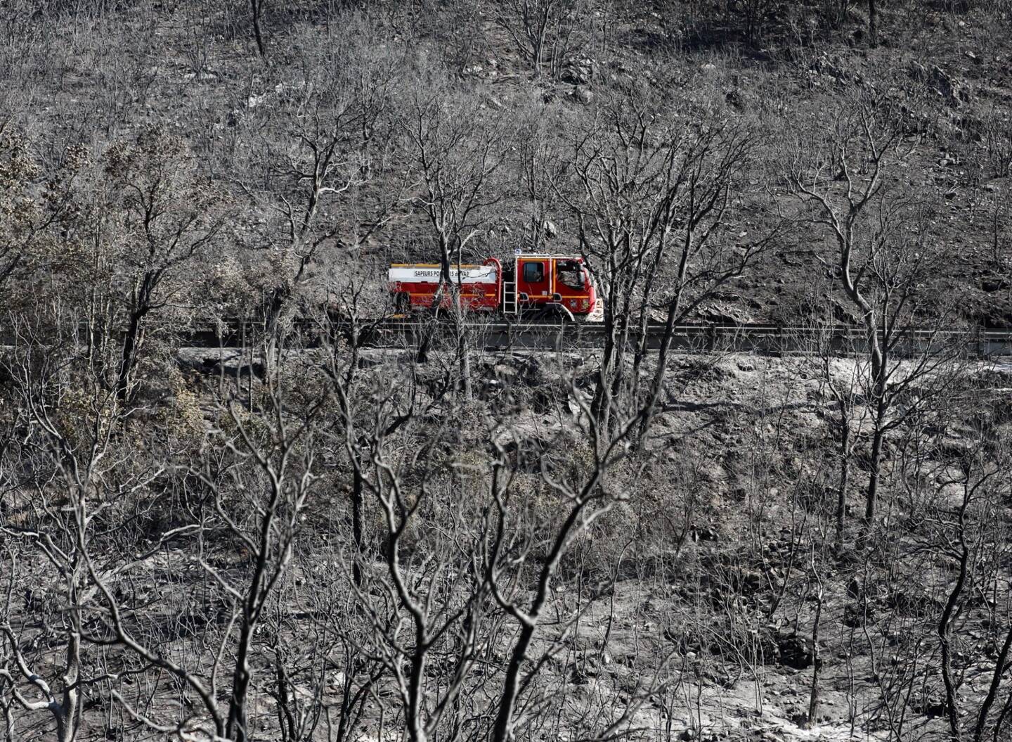 Un camion de pompiers traverse un paysage brûlé, calciné. 
