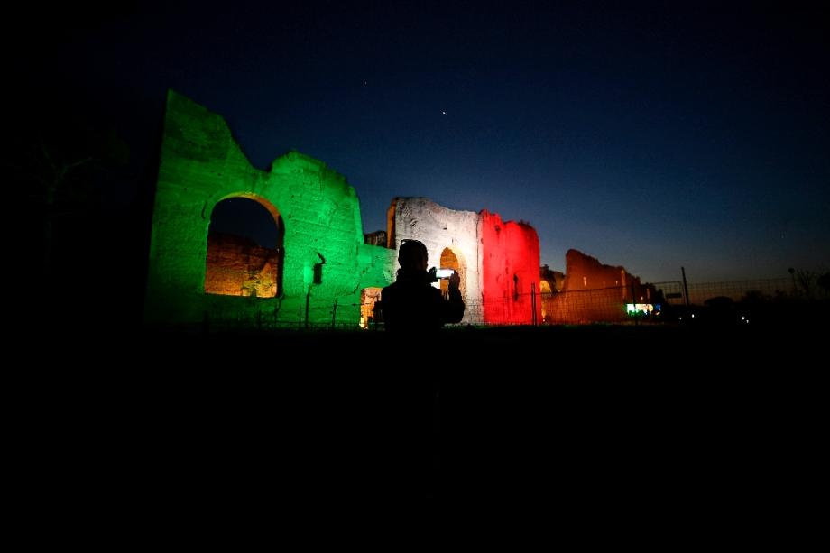 Un homme prend une photo des Thermes de Caracalla sur lesquels les couleurs du drapeau italien sont projetées, le 10 avril 2020 à Rome