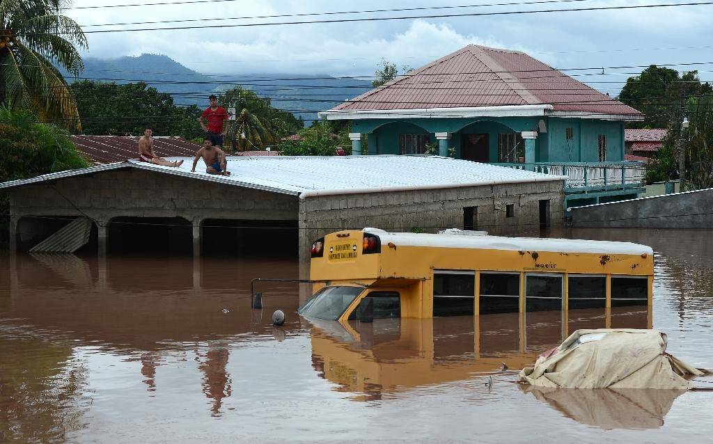 Des habitants réfugiés sur le toit d'un bâtiment près d'un bus submergé par les eaux, le 6 novembre 2020 à El Progreso, au Honduras