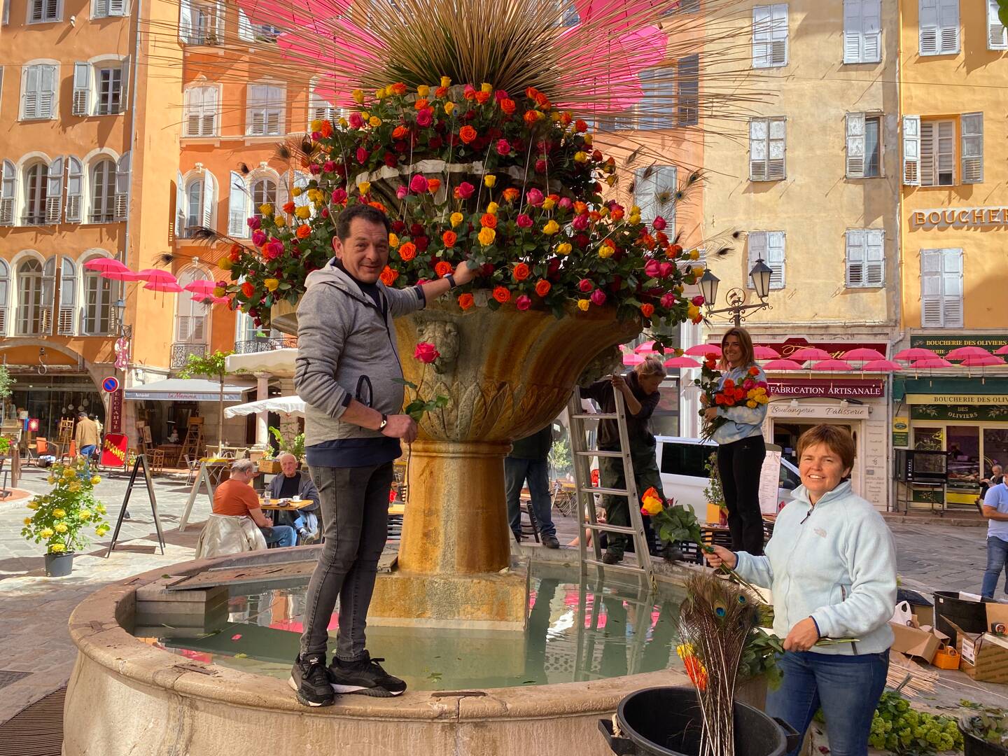 La fontaine de la place aux Aires piquée de roses oranges et jaunes lors des derniers préparatifs.